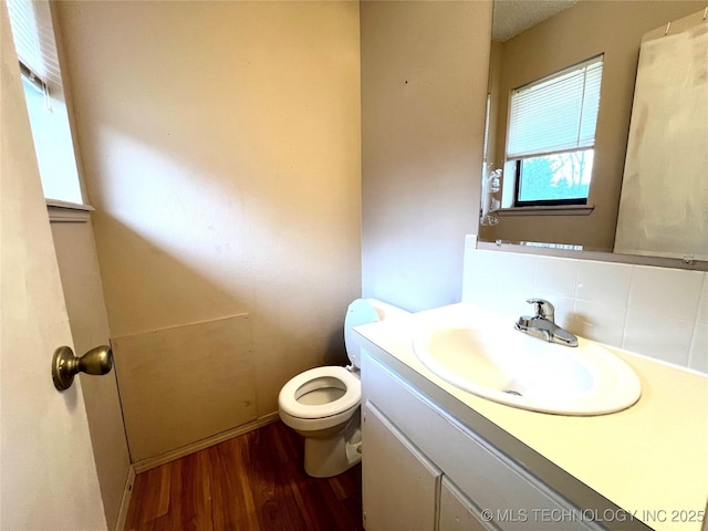 half bathroom featuring toilet, decorative backsplash, wood finished floors, and vanity