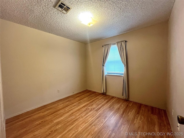 spare room with a textured ceiling, light wood-type flooring, and visible vents