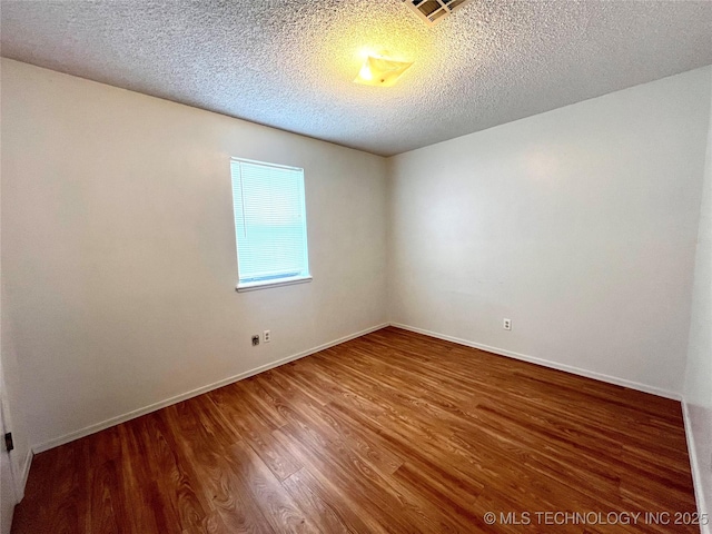 spare room featuring a textured ceiling, wood finished floors, visible vents, and baseboards