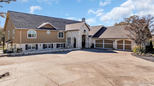 view of front of property with roof with shingles, a chimney, concrete driveway, an attached garage, and stone siding