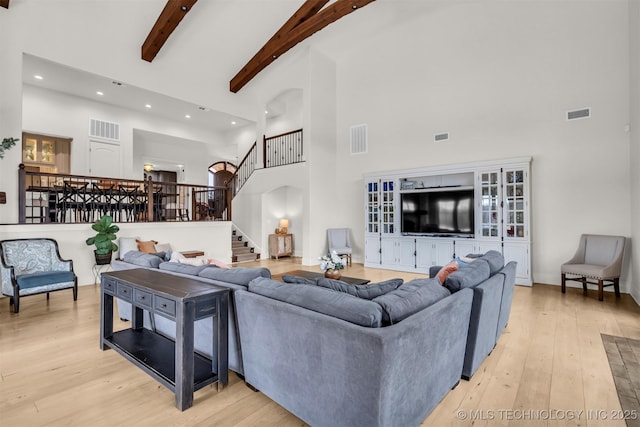 living area with a towering ceiling, light wood-style floors, stairs, and visible vents