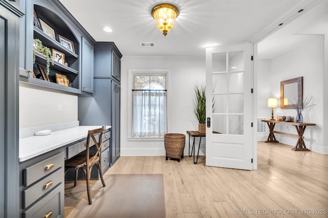 home office with light wood-style flooring, visible vents, baseboards, ornamental molding, and built in desk