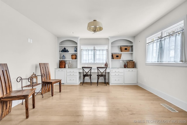 living area with built in shelves, light wood finished floors, visible vents, built in study area, and baseboards