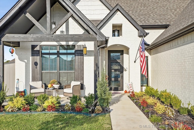 view of exterior entry featuring brick siding, a porch, and a shingled roof