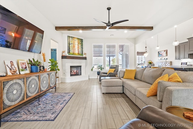 living room with vaulted ceiling with beams, ceiling fan, light wood-type flooring, a warm lit fireplace, and baseboards