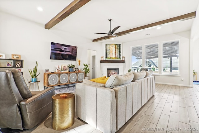 living room featuring a ceiling fan, baseboards, light wood-style floors, a lit fireplace, and beamed ceiling