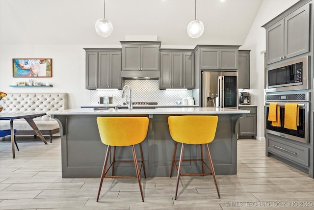 kitchen with a kitchen island with sink, stainless steel appliances, decorative backsplash, and gray cabinetry