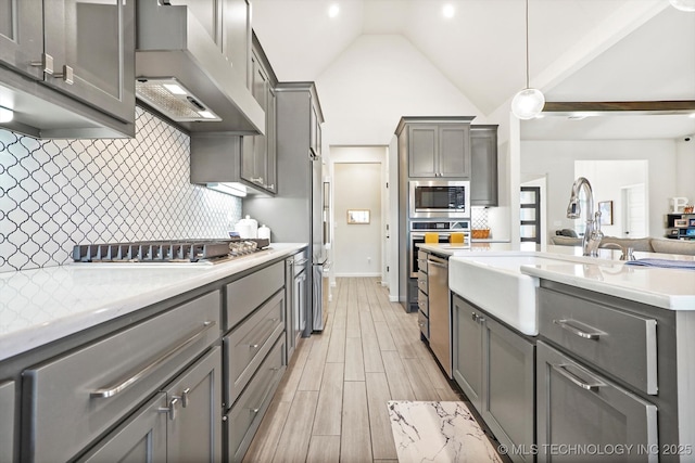 kitchen featuring gray cabinets, light countertops, appliances with stainless steel finishes, a sink, and wall chimney exhaust hood