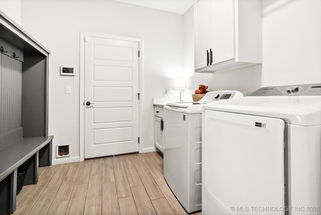 washroom with cabinet space, washing machine and dryer, baseboards, and light wood-style floors