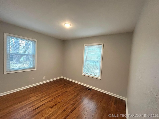 unfurnished room with dark wood-type flooring, visible vents, and baseboards