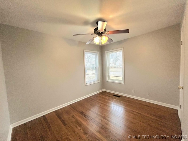 unfurnished room with dark wood-type flooring, visible vents, baseboards, and a ceiling fan