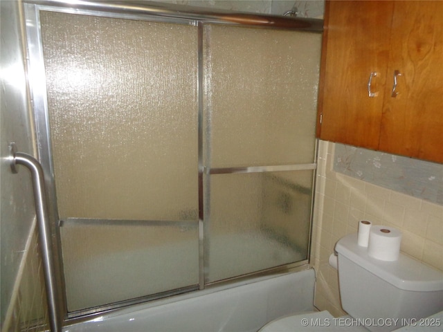 full bathroom featuring bath / shower combo with glass door, toilet, and tile walls