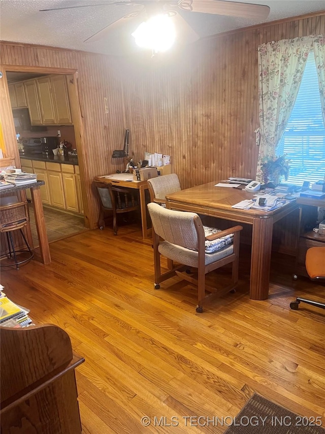 dining room with ceiling fan, wooden walls, and light wood-style floors