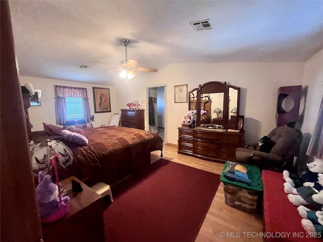 bedroom with a ceiling fan, a textured ceiling, visible vents, and wood finished floors