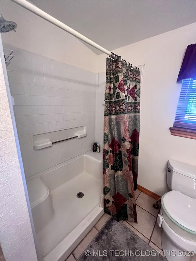 bathroom with a stall shower, baseboards, tile patterned flooring, and toilet