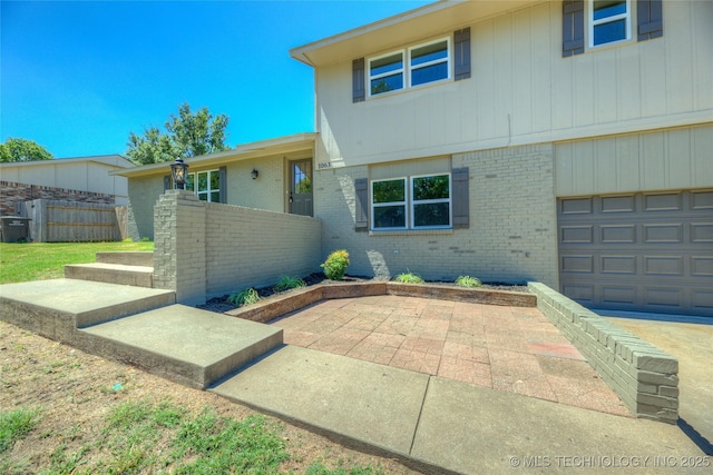 view of front facade with an attached garage, fence, a patio, and brick siding