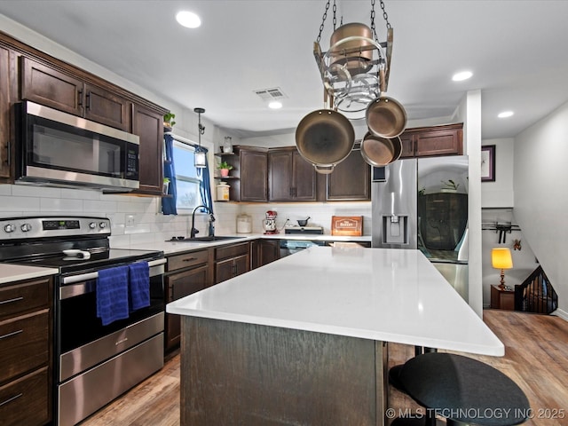 kitchen with light wood-style floors, dark brown cabinets, appliances with stainless steel finishes, light countertops, and tasteful backsplash