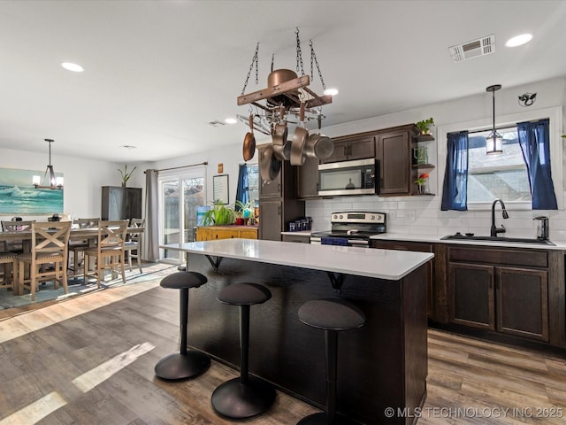 kitchen featuring stainless steel appliances, wood finished floors, a sink, visible vents, and backsplash