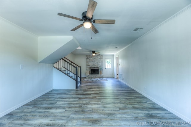 unfurnished living room with crown molding, visible vents, a stone fireplace, wood finished floors, and baseboards