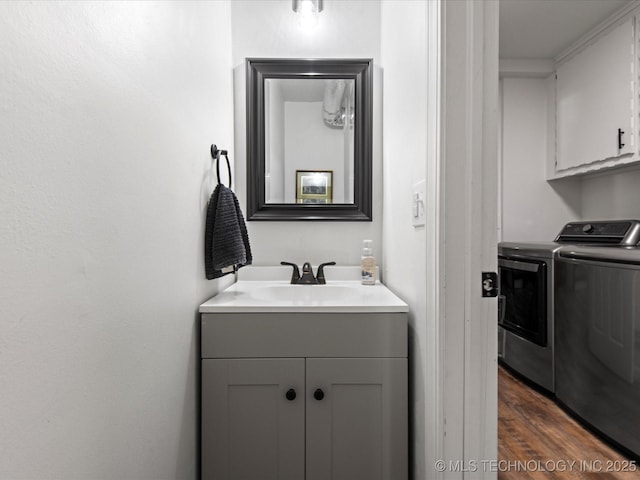 clothes washing area featuring dark wood finished floors, washer and clothes dryer, a sink, and cabinet space