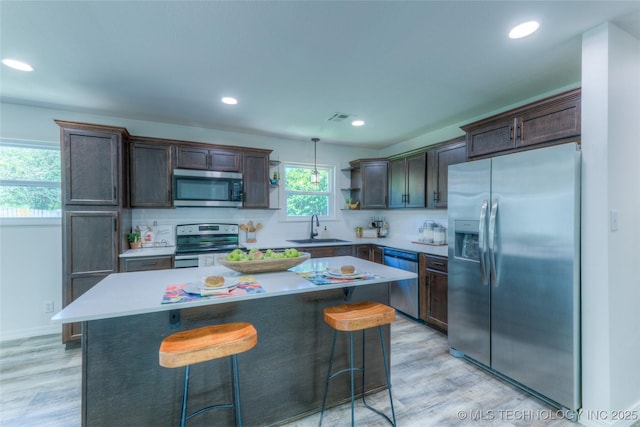 kitchen with light wood finished floors, stainless steel appliances, visible vents, a sink, and a center island