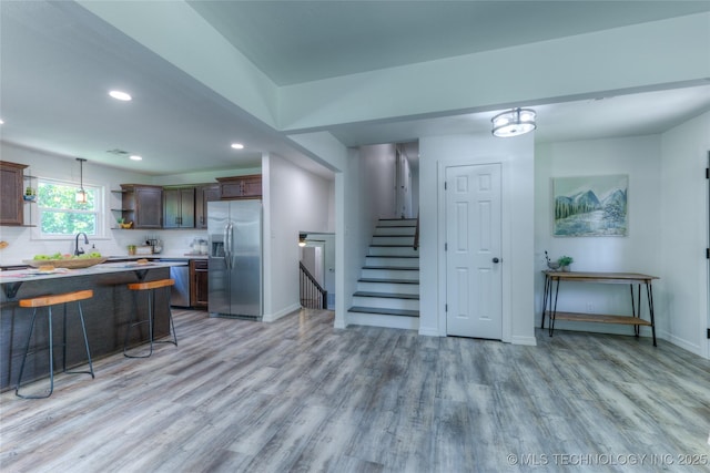 kitchen featuring recessed lighting, a kitchen breakfast bar, open shelves, light wood-style flooring, and appliances with stainless steel finishes