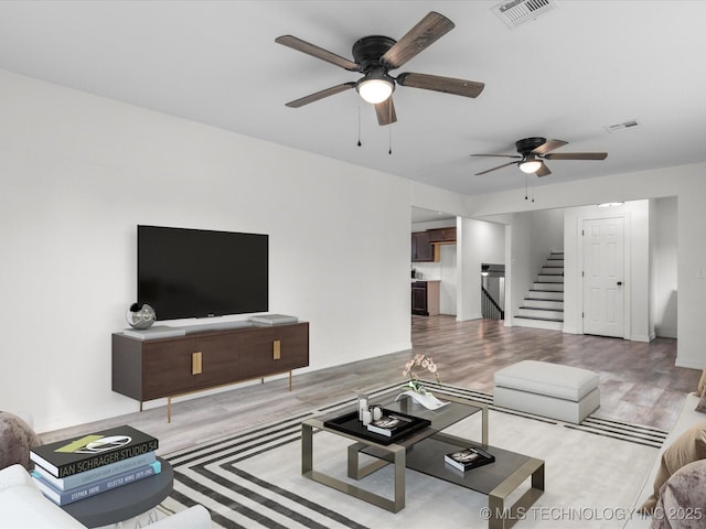 living room with stairway, light wood-style flooring, visible vents, and ceiling fan