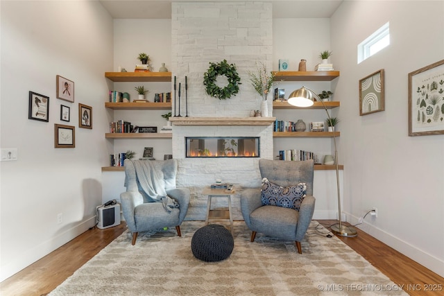 sitting room with built in shelves, a fireplace, wood finished floors, and baseboards