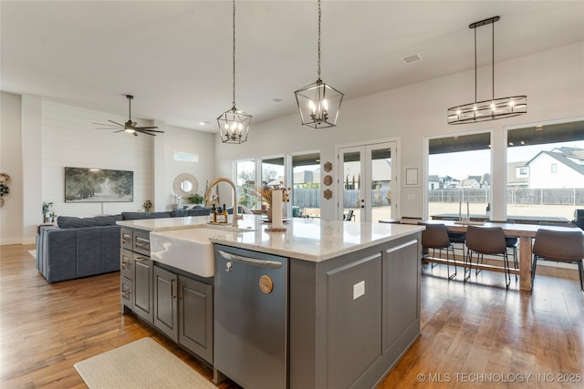 kitchen featuring stainless steel dishwasher, open floor plan, a kitchen island with sink, a sink, and wood finished floors