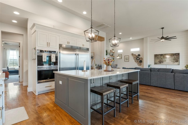 kitchen featuring decorative light fixtures, stainless steel appliances, white cabinets, wood finished floors, and a kitchen bar