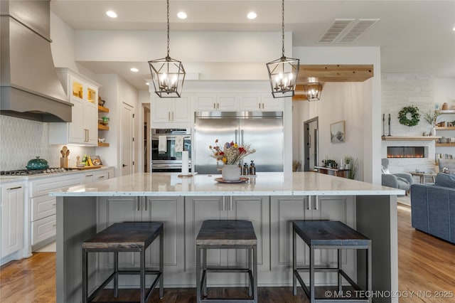 kitchen featuring visible vents, white cabinets, custom range hood, wood finished floors, and stainless steel appliances