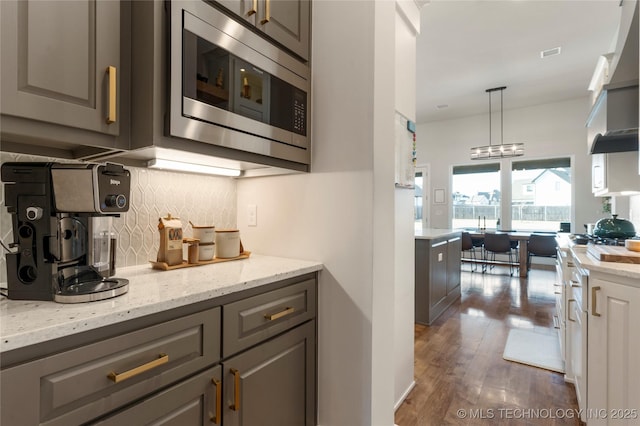 kitchen featuring light stone counters, dark wood finished floors, tasteful backsplash, stainless steel microwave, and wall chimney exhaust hood