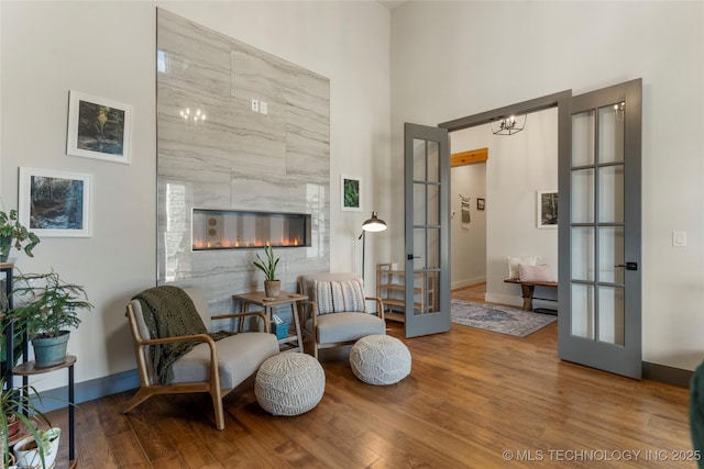 sitting room with a premium fireplace, wood finished floors, a towering ceiling, baseboards, and french doors