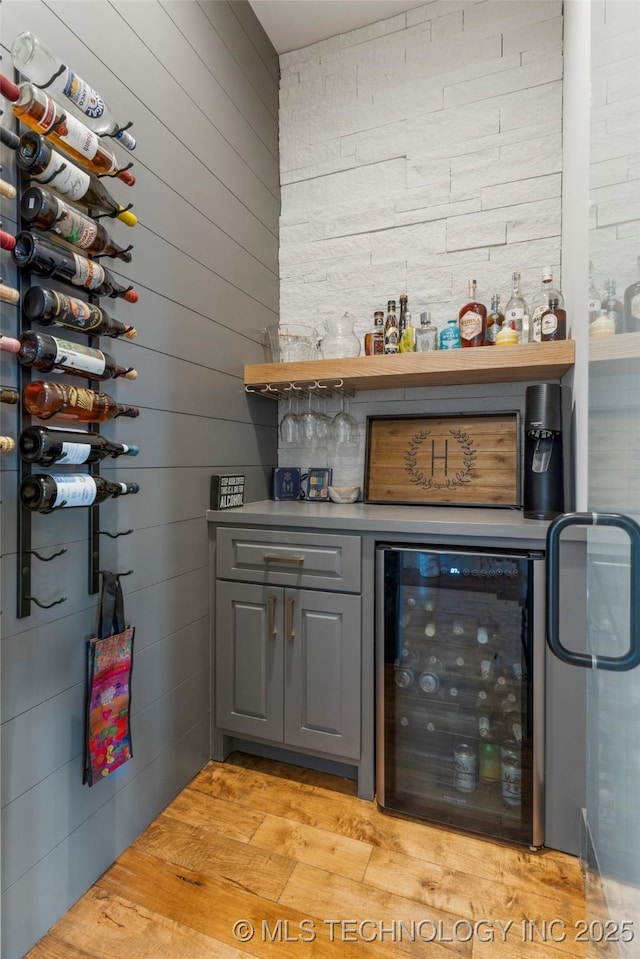 bar featuring light wood-type flooring, beverage cooler, wood walls, and a bar