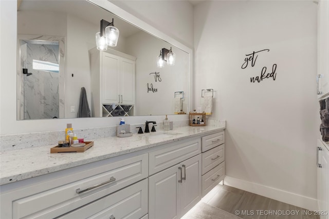 bathroom featuring a marble finish shower, baseboards, and vanity