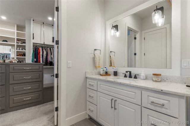 bathroom with a spacious closet, vanity, and baseboards