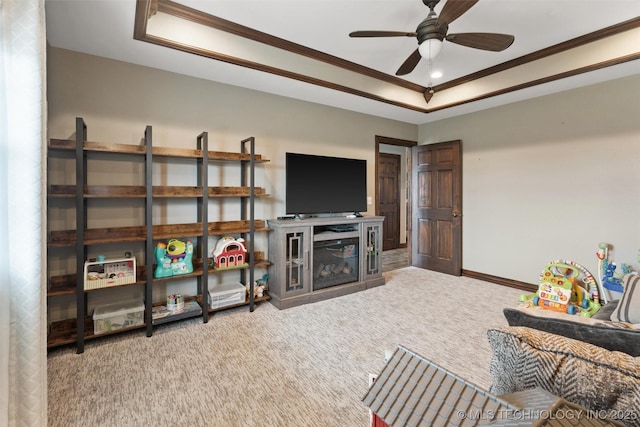 carpeted living room featuring a ceiling fan, baseboards, a tray ceiling, and crown molding