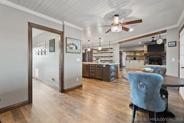 dining area featuring a fireplace, baseboards, ornamental molding, light wood finished floors, and indoor wet bar