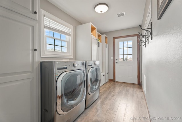 clothes washing area with light wood-style flooring, visible vents, baseboards, cabinet space, and washing machine and clothes dryer