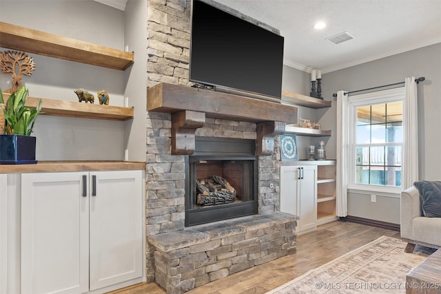 living room featuring light wood finished floors, baseboards, visible vents, a fireplace with raised hearth, and ornamental molding