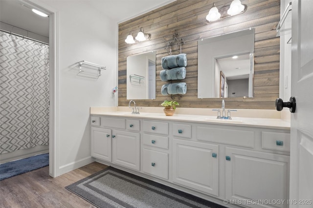 full bathroom featuring wood finished floors, a sink, wooden walls, and double vanity