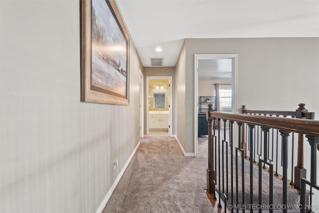 hallway with an upstairs landing, carpet flooring, visible vents, and baseboards
