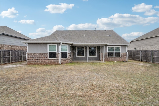 back of house featuring brick siding, a lawn, and a fenced backyard