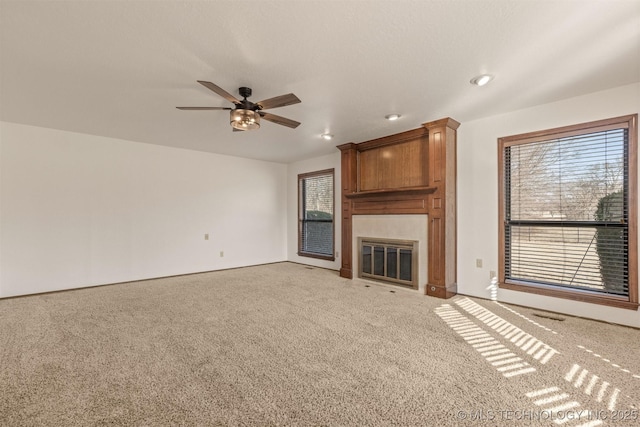 unfurnished living room with a ceiling fan, a fireplace, a wealth of natural light, and light colored carpet