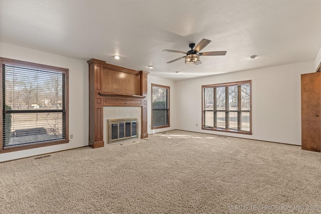 unfurnished living room featuring a large fireplace, visible vents, a ceiling fan, light colored carpet, and a textured ceiling