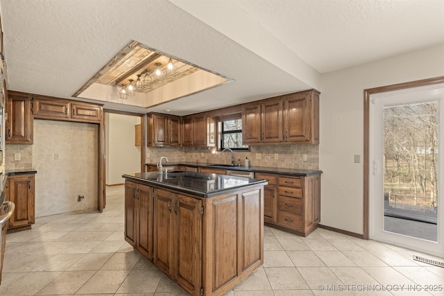 kitchen with tasteful backsplash, visible vents, a raised ceiling, a kitchen island with sink, and a sink