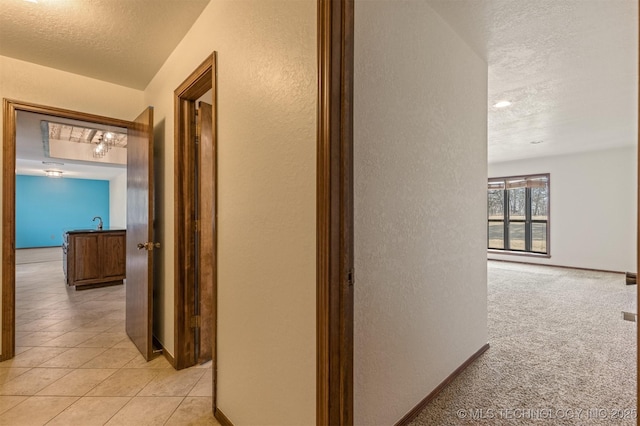 hall with light carpet, baseboards, a textured wall, a textured ceiling, and light tile patterned flooring