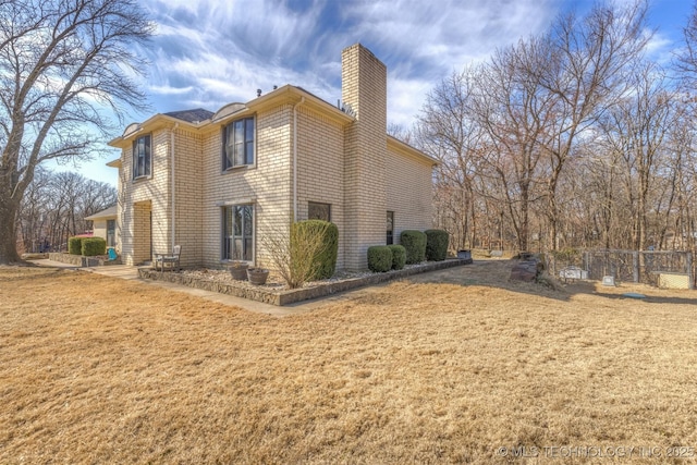 view of side of home with a yard, brick siding, a chimney, and fence