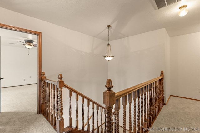 hallway with a textured ceiling, carpet flooring, visible vents, an upstairs landing, and baseboards