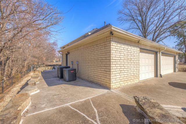 view of side of property featuring a garage, brick siding, and central AC unit